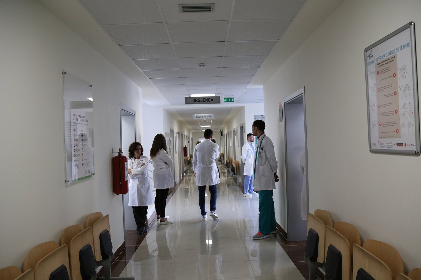 A bright corridor in a renovated health centre in Patos, Albania, with medical staff in white coats walking away from the camera and waiting chairs along the walls.