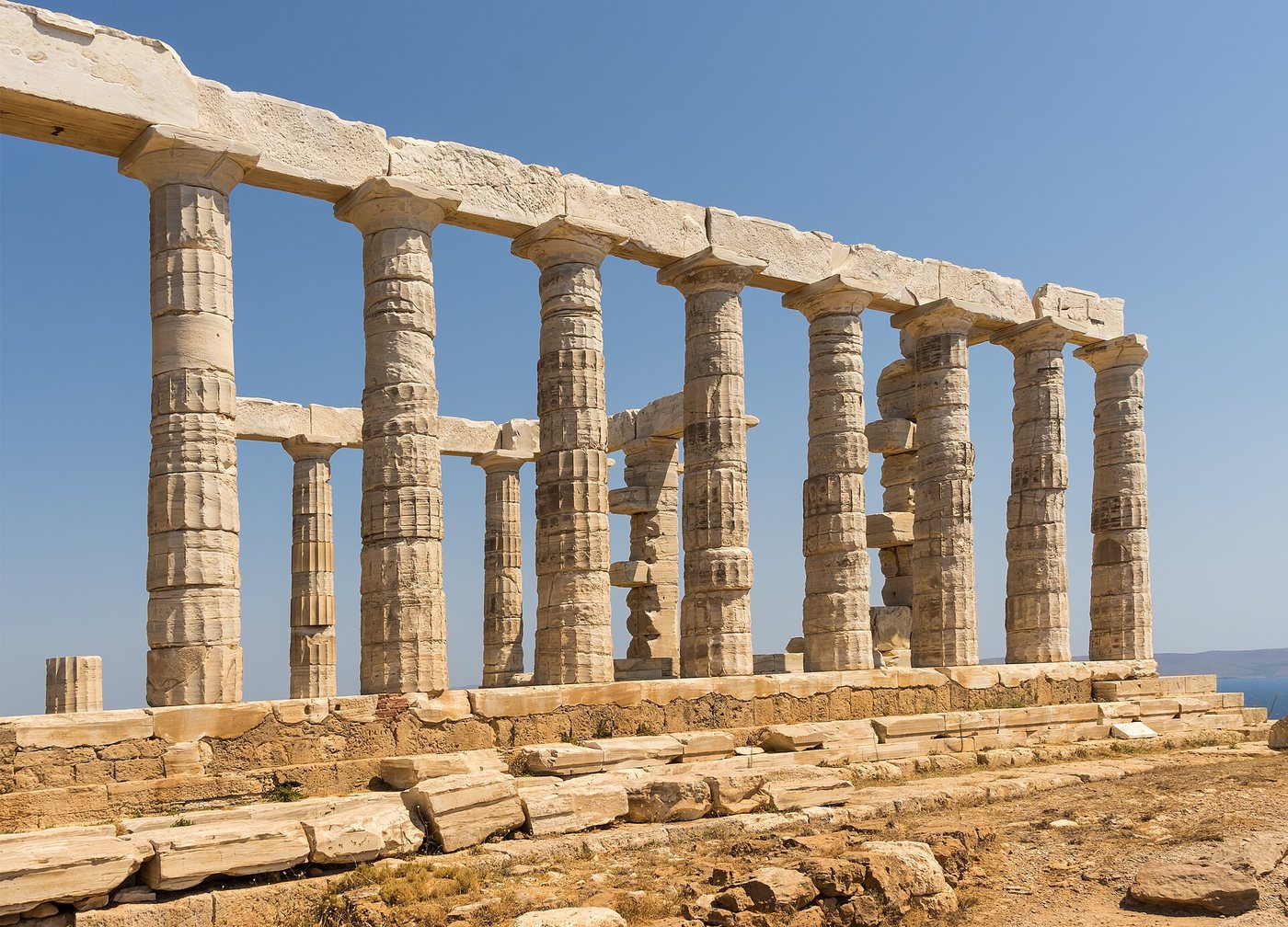 Weathered Doric marble columns of the Temple of Poseidon at Cape Sounion, Greece, seen in perspective against a clear blue sky.